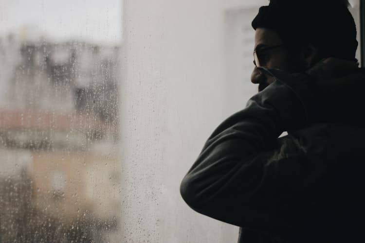 Man looking outside rainy window.