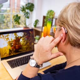Woman touches hearing aid behind ear