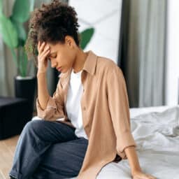 Woman with tinnitus sitting on the bed with her hand on her forehead