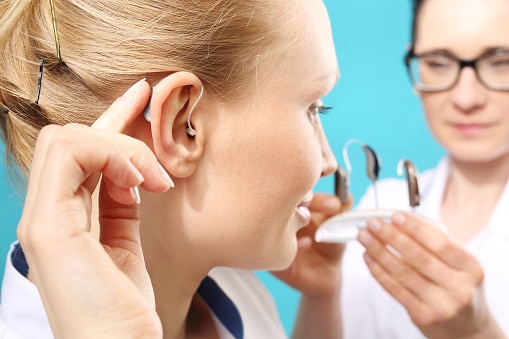 A patient tries on their new hearing aids with the help of an audiologist.