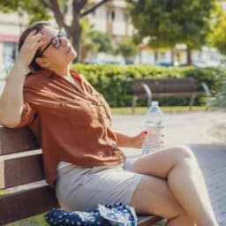 Displeased woman eyes closed sitting on a park bench holding a water bottle.